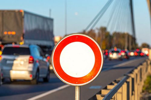 KI-generierte Abbildung. Im Vordergrund ein "Durchfahrt verboten" Schild und im Hintergrund leuchtende Rücklichter von Autos auf einer Straße. 