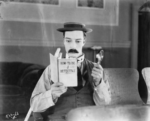 Buster Keaton liest das Buch "How to be a detective". In der Hand hält er eine Lupe.