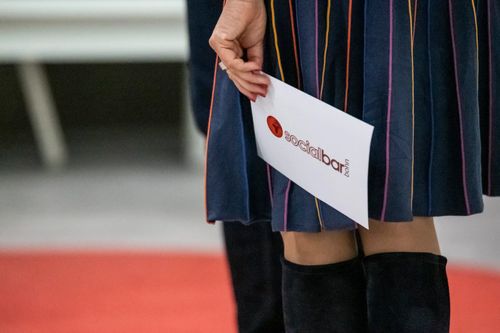 79. Socialbar Bonn.
Eine Person, die einen Flyer von der Socialbar Bonn in der Hand hält.